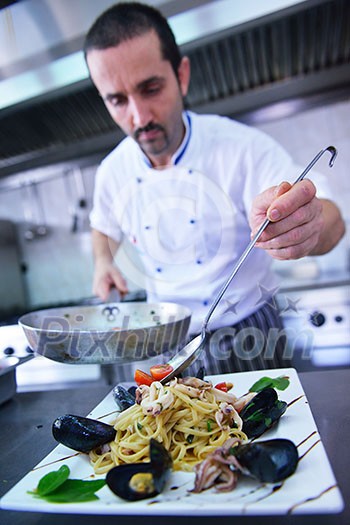Handsome chef dressed in white uniform decorating pasta salad and seafood fish in modern kitchen Handsome chef dressed in white uniform decorating pasta salad and seafood fish in modern kitchen