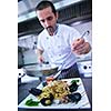 Handsome chef dressed in white uniform decorating pasta salad and seafood fish in modern kitchen