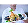 Handsome chef dressed in white uniform decorating pasta salad and seafood fish in modern kitchen