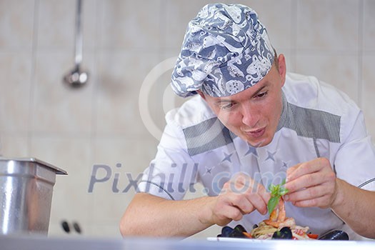 Handsome chef dressed in white uniform decorating pasta salad and seafood fish in modern kitchen