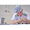 Handsome chef dressed in white uniform decorating pasta salad and seafood fish in modern kitchen