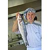 Handsome chef dressed in white uniform decorating pasta salad and seafood fish in modern kitchen