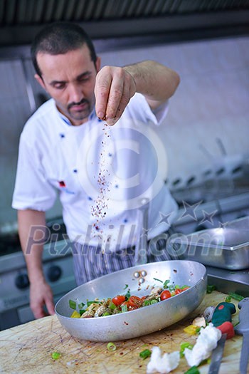 Handsome chef dressed in white uniform decorating pasta salad and seafood fish in modern kitchen