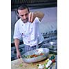 Handsome chef dressed in white uniform decorating pasta salad and seafood fish in modern kitchen