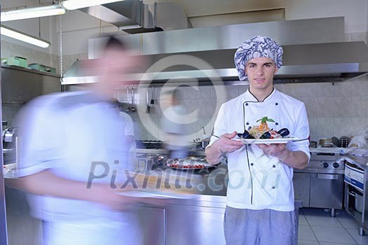 Handsome chef dressed in white uniform decorating pasta salad and seafood fish in modern kitchen