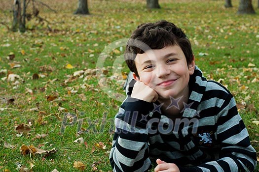 Cute boy  in autumn park laying on grass 