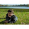 Cute boy  in autumn park laying on grass 