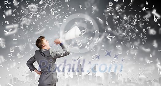 Young excited businessman screaming in paper trumpet