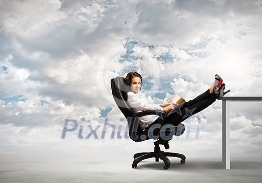 Young businesswoman sitting in chair with legs on table and reading book Young businesswoman sitting in chair with legs on table and reading book