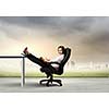 Young businesswoman sitting in chair with legs on table and reading book