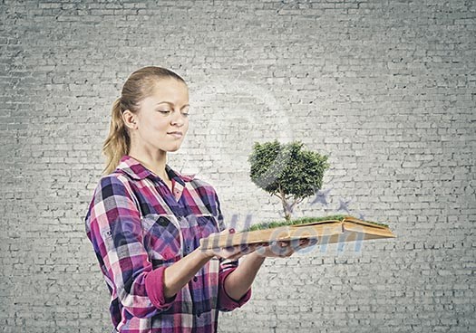 Young woman in casual holding opened book with green tree Young woman in casual holding opened book with green tree