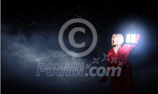 Young woman in red cloak with lantern lost in forest