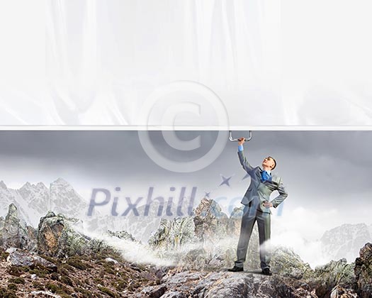 Image of young businessman pulling blank banner from above Image of young businessman pulling blank banner from above