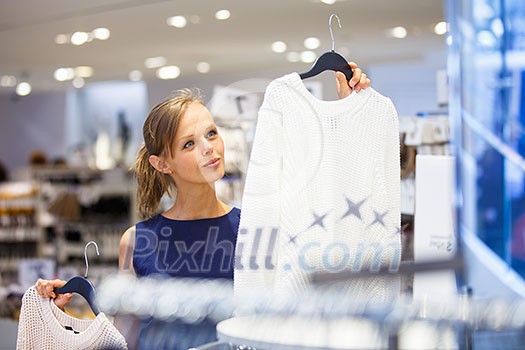 Beautiful young female shopper in a clothing store, chossing a blouse/t-shirt/garments (shallow DOF; color toned image)