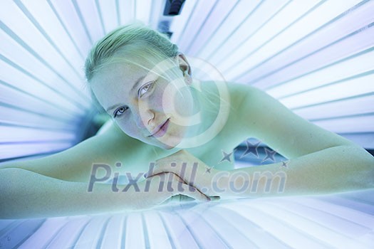 Pretty, young woman tanning her skin in a modern solarium/sunbed. Getting an energy boost during dark winter days.