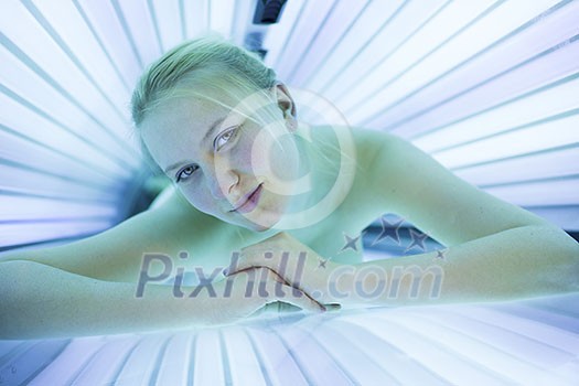 Pretty, young woman tanning her skin in a modern solarium/sunbed. Getting an energy boost during dark winter days. Pretty, young woman tanning her skin in a modern solarium/sunbed. Getting an energy boost during dark winter days.