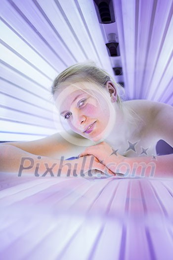 Pretty, young woman tanning her skin in a modern solarium/sunbed. Getting an energy boost during dark winter days.