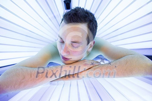 Handsome young man relaxing during a tanning session in a modern solarium, taking care of himself, enjoying the artificial sunlight. Handsome young man relaxing during a tanning session in a modern solarium, taking care of himself, enjoying the artificial sunlight.
