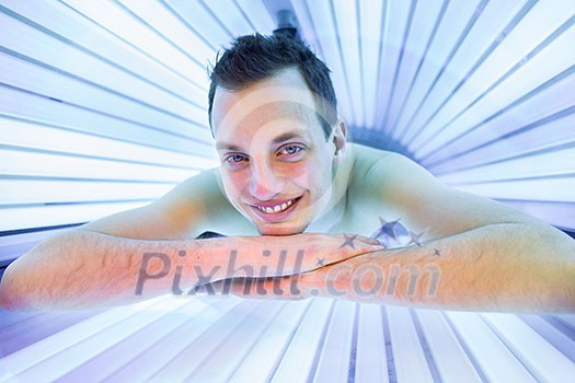 Handsome young man relaxing during a tanning session in a modern solarium, taking care of himself, enjoying the artificial sunlight. Handsome young man relaxing during a tanning session in a modern solarium, taking care of himself, enjoying the artificial sunlight.