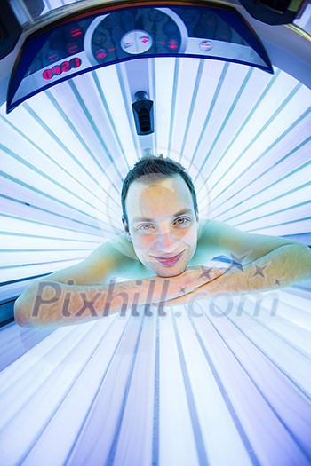 Handsome young man relaxing during a tanning session in a modern solarium, taking care of himself, enjoying the artificial sunlight.