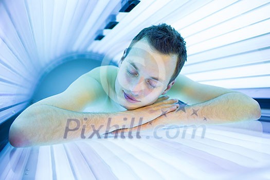 Handsome young man relaxing during a tanning session in a modern solarium, taking care of himself, enjoying the artificial sunlight. Handsome young man relaxing during a tanning session in a modern solarium, taking care of himself, enjoying the artificial sunlight.