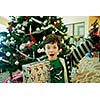 Smiling boy with giftbox looking at camera out of decorated firtree