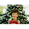 Smiling boy with giftbox looking at camera out of decorated firtree