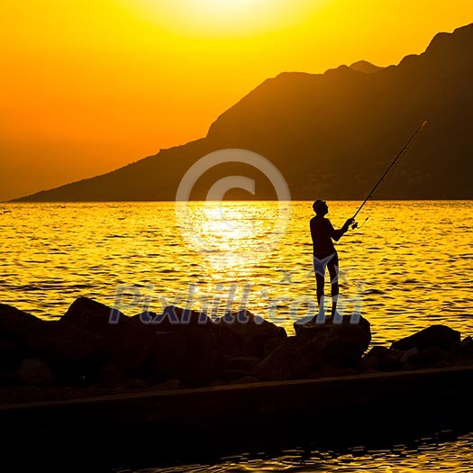 Fisherman silhouette on the beach at colorful sunset