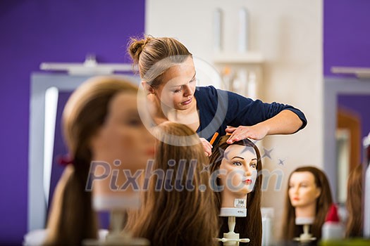Pretty female hairdresser/haidressing apprentice/student training on an apprentice head