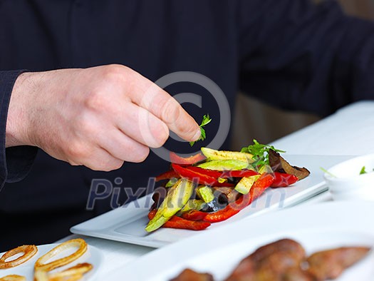 Handsome chef dressed in black uniform decorating tasty food in restaurant