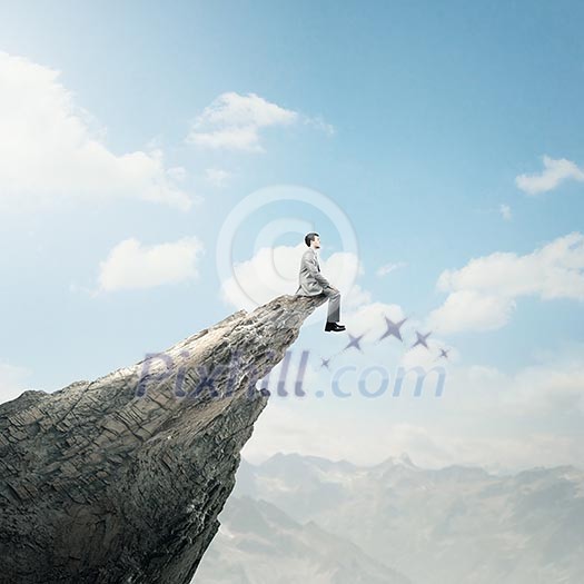 Young businessman sitting on edge of rock