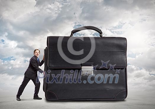 Young businessman making effort to move macro suitcase