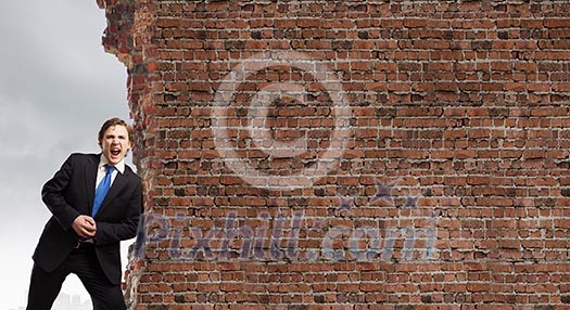 Young businessman making effort to move brick wall