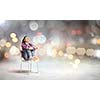 Young woman sitting on chair with bokeh lights at background