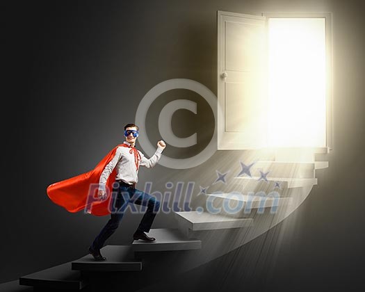 Young confident superman in mask and cape walking on ladder
