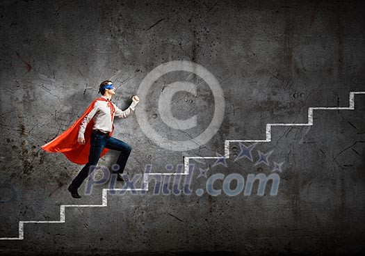 Young confident superman in mask and cape walking on ladder Young confident superman in mask and cape walking on ladder