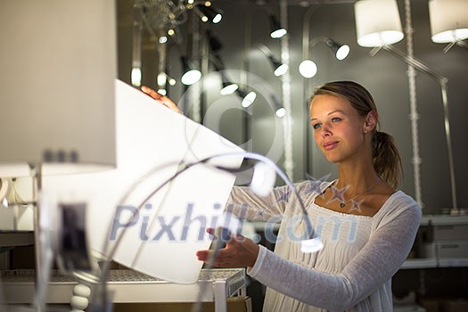 Pretty, young woman choosing the right light for her apartment in a modern home furnishings store (color toned image; shallow DOF) Pretty, young woman choosing the right light for her apartment in a modern home furnishings store (color toned image; shallow DOF)