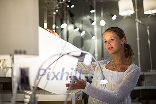 Pretty, young woman choosing the right light for her apartment in a modern home furnishings store (color toned image; shallow DOF)