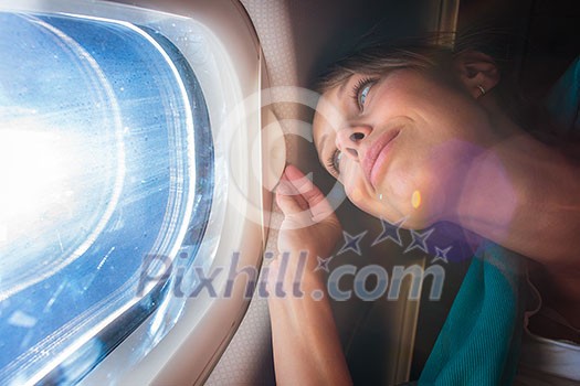 Happy, female airplane passanger enjoying the view from the cabon window over the blue sky (shallow DOF; intentional flare)