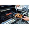 BBQ with sausages and red meat on the grill - male hands holding a plate and taking the meat off the grill before it is too late