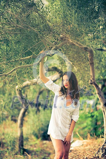 Attractive, young brunette on the beach, amid olive trees, looking both sensual and natural