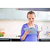 Pretty, young woman with her morning coffee and a tablet computer in modern kitchen - checking e-mails, reading news first thing in the morning