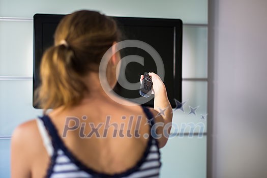 Young woman at home watching TV, turning it on, changing channels