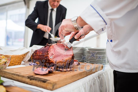 Catering service employee cutting ham for people during an event