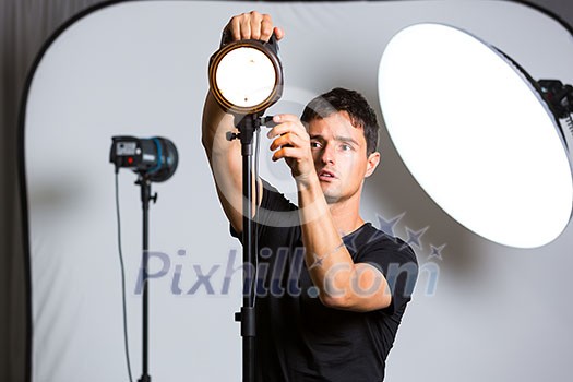Young pro photographer in his studio setting up lights for the upcoming photoshoot (color toned image; shallow DOF)