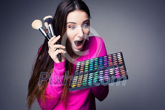 Cute make-up artist holding her vast palette of colors and hands with brushes around her (color toned image) Cute make-up artist holding her vast palette of colors and hands with brushes around her (color toned image)