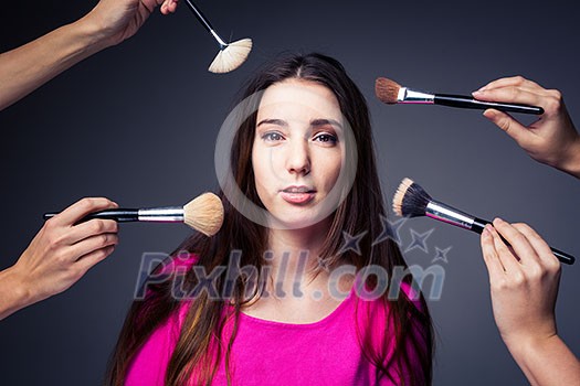 Pretty, young woman in the able care of professional make-up artists (color toned image) - hands with brushes around her, she is going to look awesome