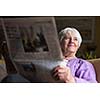 Senior woman reading morning newspaper, sitting in her favorite chair in her living room, looking happy