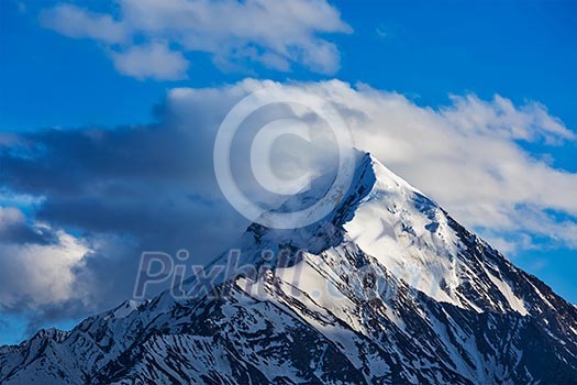 Snowcapped summit top of mountain in Himalayas in clouds. Himachal Pradesh, India Snowcapped summit top of mountain in Himalayas in clouds. Himachal Pradesh, India
