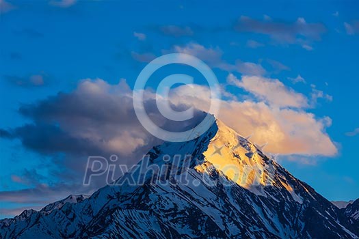 Snowcapped summit top of mountain in Himalayas in clouds on sunset. Himachal Pradesh, India